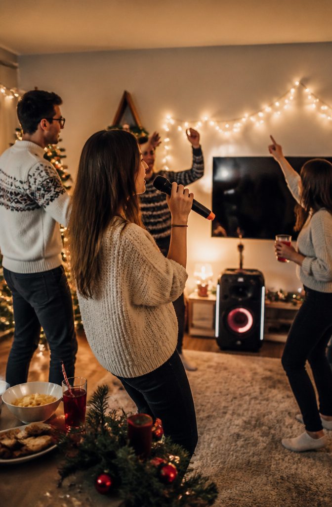 15 Xmas Party Ideas & Games for 2026 Celebrations 13 A group singing karaoke in a festively decorated living room.